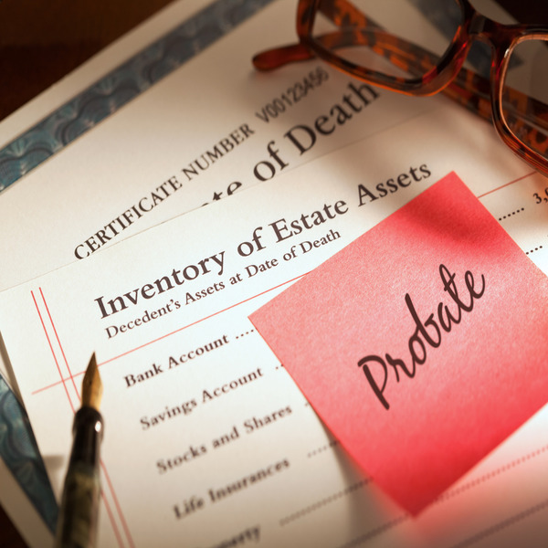 Close-up of death certificate and inventory of estate paper with eyeglasses, a pen, and a pink post-it that says “probate” on it
